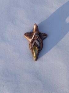 A gold pendant adorned with a leaf in the snow.