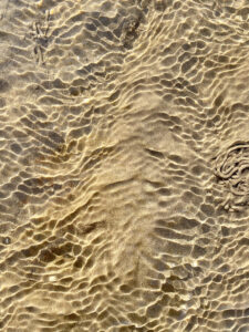 A close up of a sandy beach with ripples in the water reflecting light.
