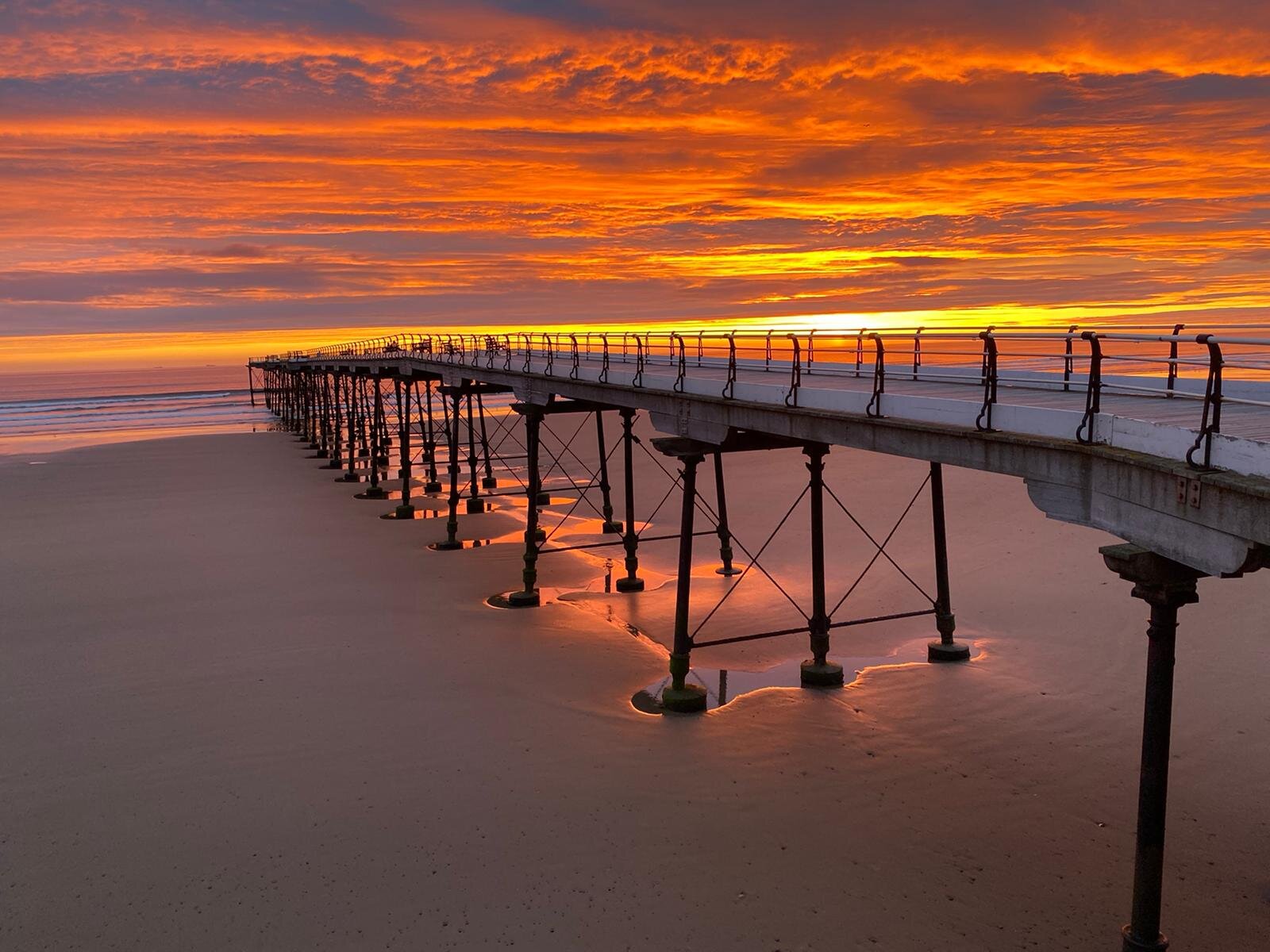 A pier on a beach with an orange sky.