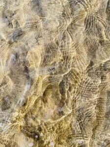 A close up of a sandy beach with ripples in the water reflecting the light.