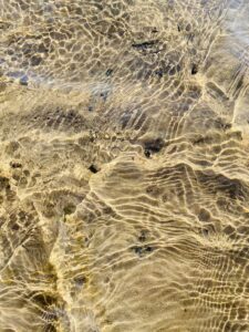 A close up of a sandy beach with ripples in the water, illuminated by the gentle light.