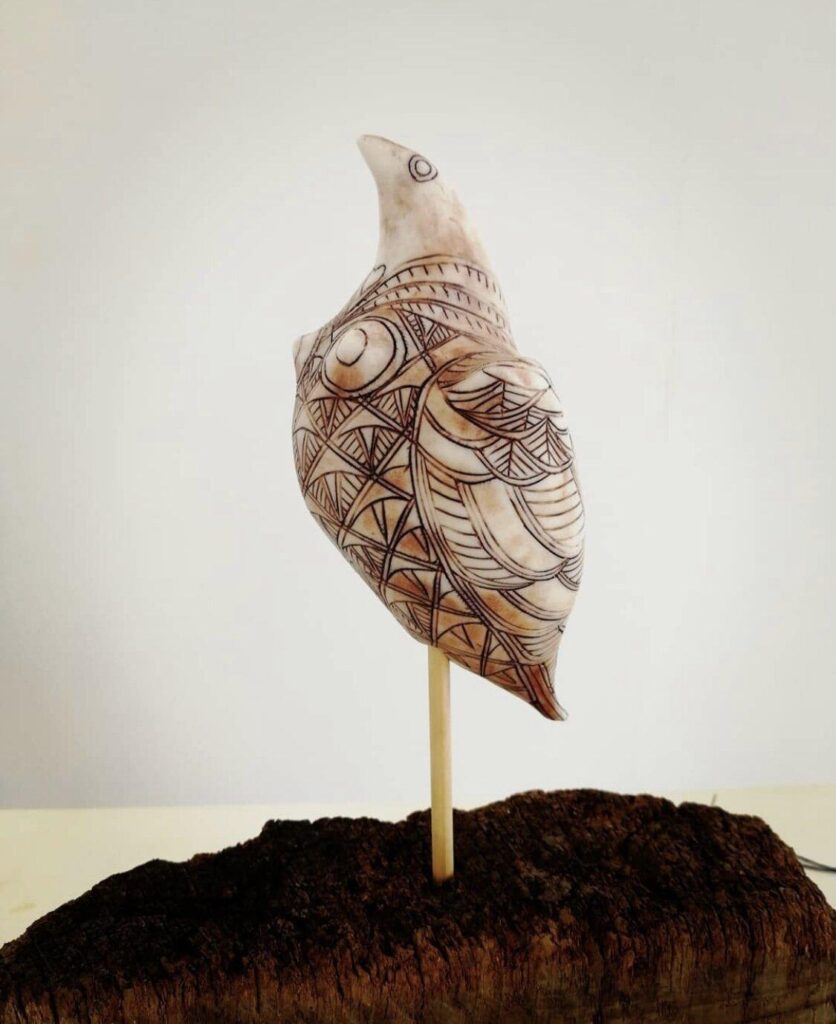 A sculpture of a bird sitting on top of a piece of wood.