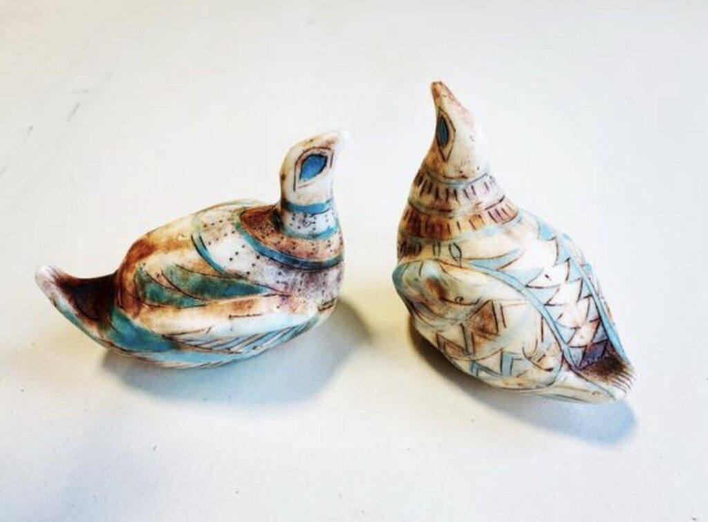 Two ceramic birds sitting on a white surface.