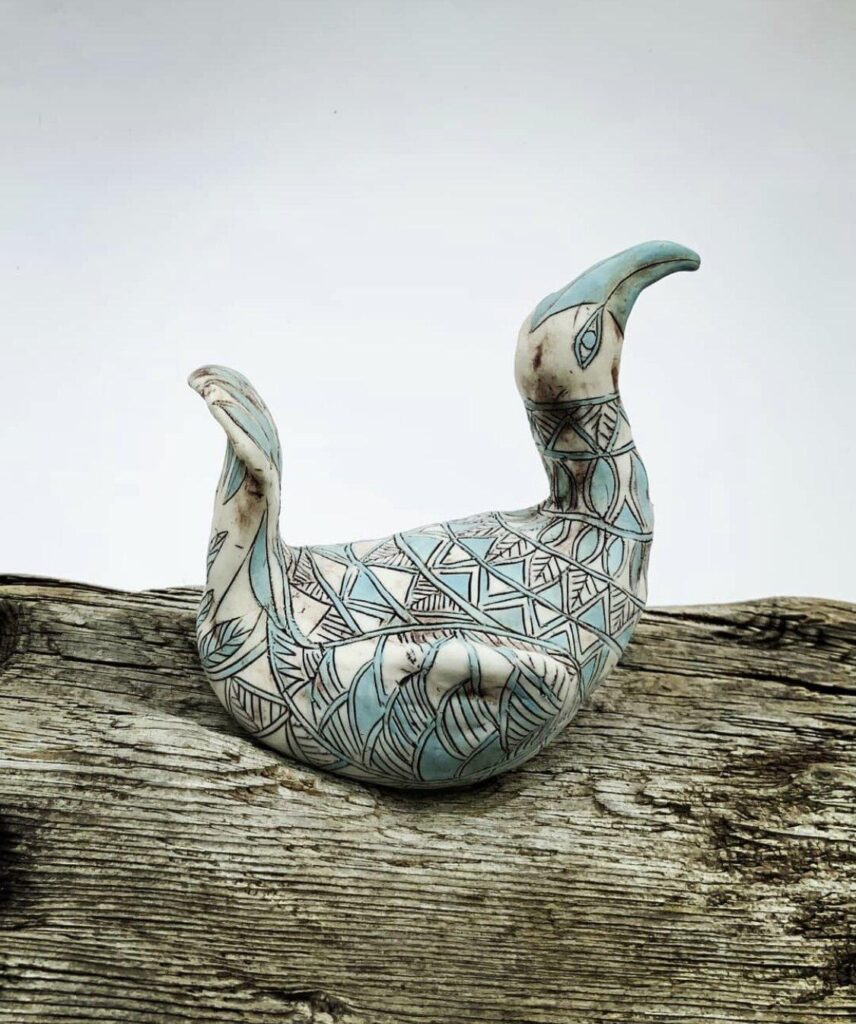 A ceramic bird sitting on top of a piece of wood.