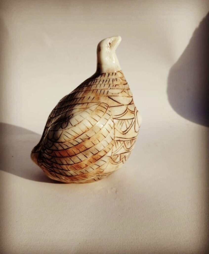 A small figurine of a pheasant sitting on a white surface.