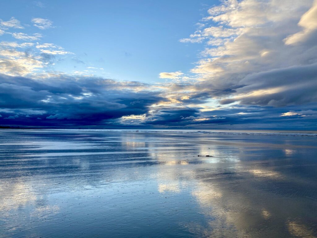 A beach with clouds reflected in the water.
