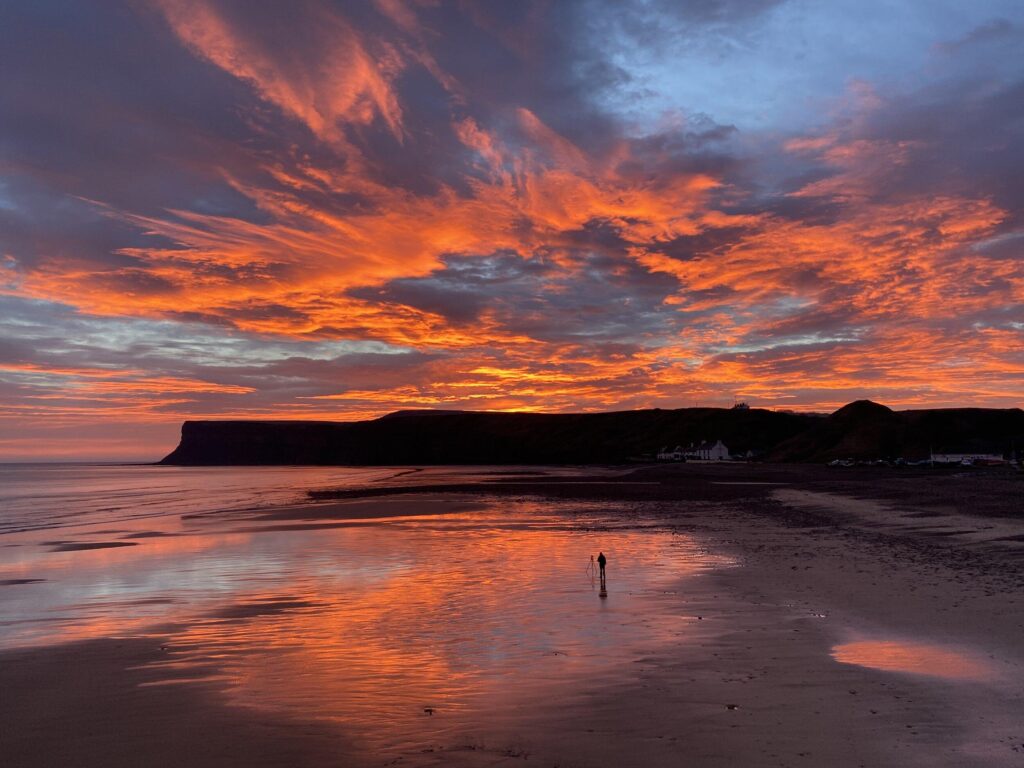 A sunset over a beach with a hill in the background.