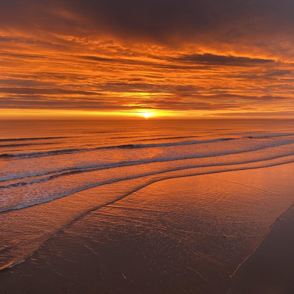 A sunset over a beach with a cloudy sky.