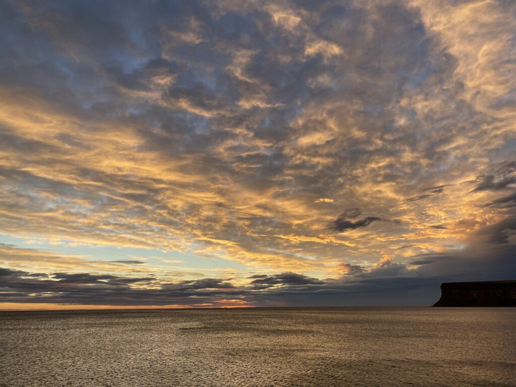 A sunset over a body of water with clouds in the sky.