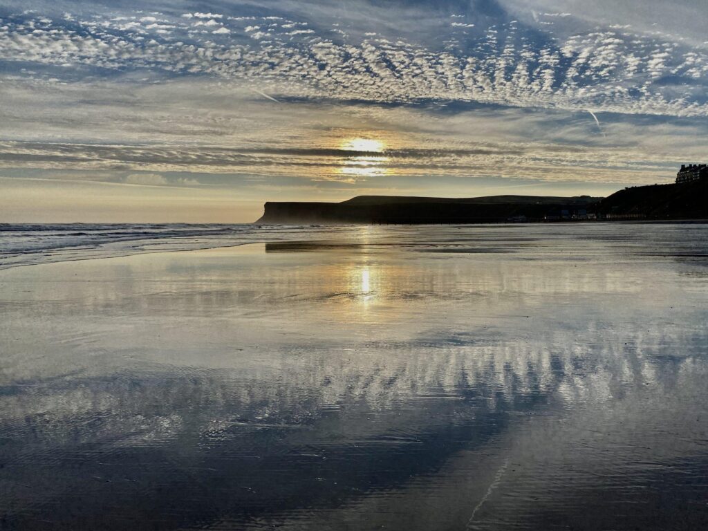 The sun is reflected in the water on a beach.