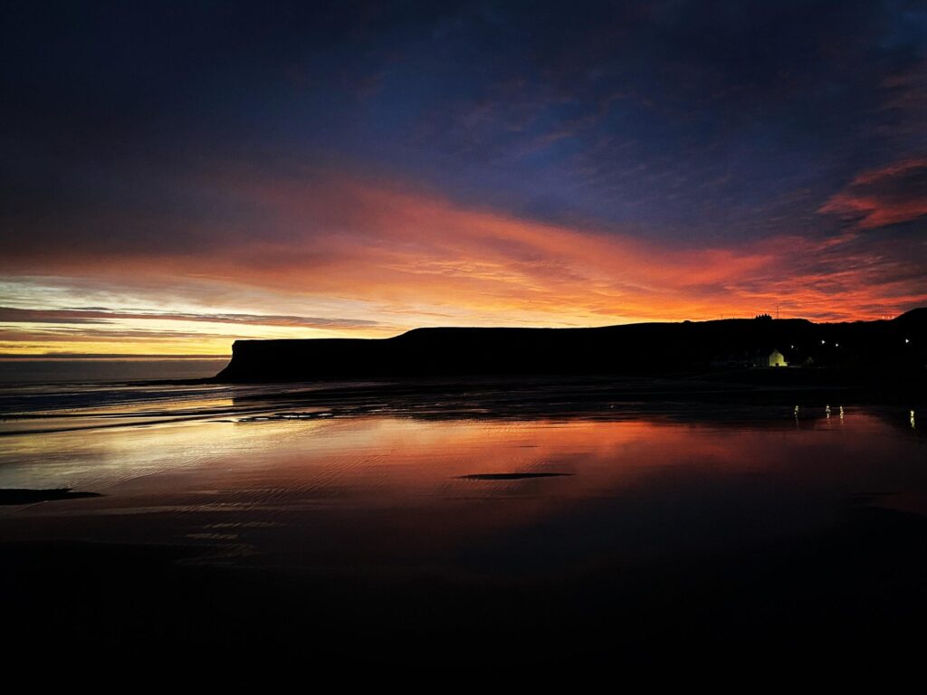 A sunset on a beach with a building in the background.