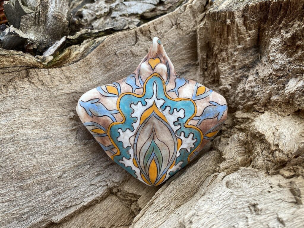 A blue and yellow painted pendant on a piece of wood.