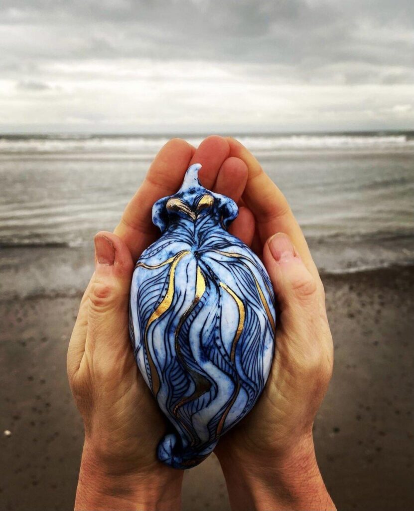 A person holding a blue and white shell on a beach.