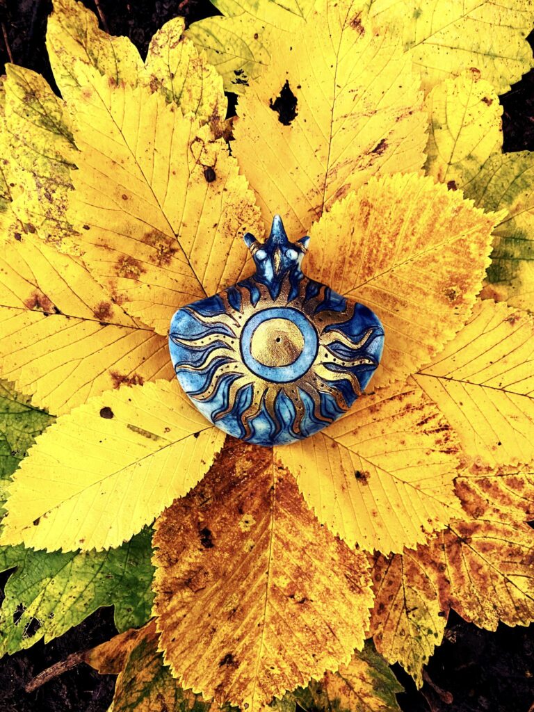 A blue sun brooch surrounded by yellow leaves.