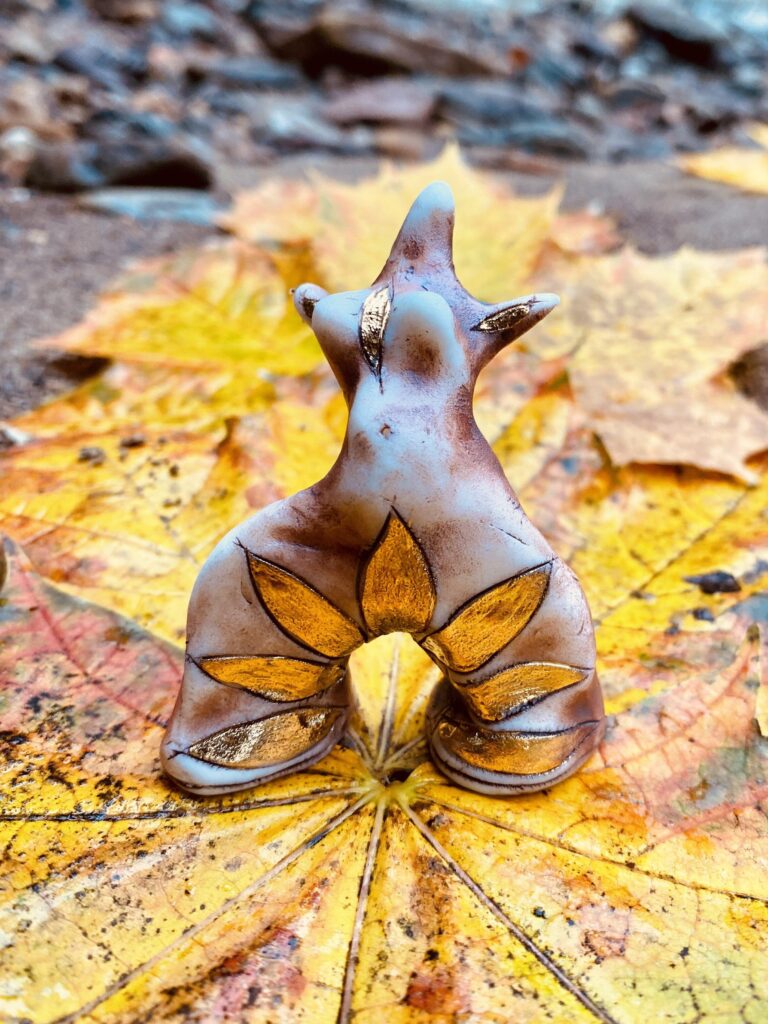 A fox figurine sitting on a pile of leaves.