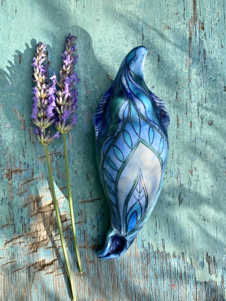 A blue ceramic dolphin with purple flowers on a wooden table.