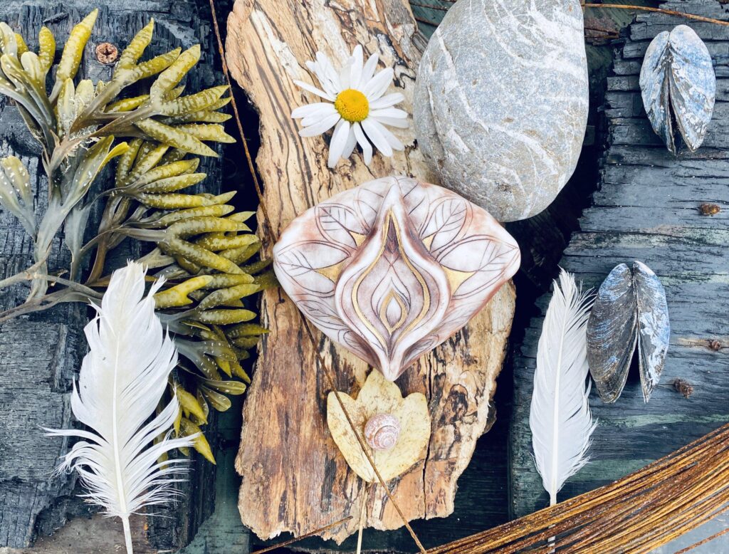Feathers, shells, and daisies are arranged on a piece of wood.