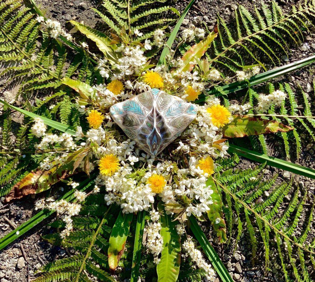 A circle of flowers and ferns on the ground.