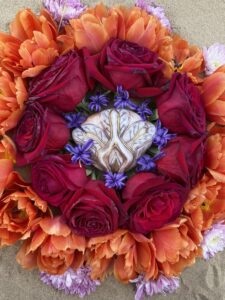 A Yoni Mandala featuring a circular arrangement of orange and red flowers on the sand.