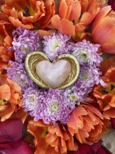 A Yoni Mandala with a heart-shaped crystal and orange and pink tulips.