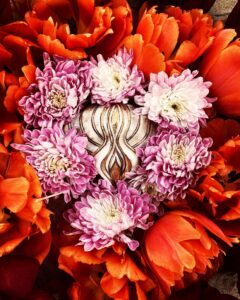 A Yoni Mandala of orange and pink flowers shaped like a heart.