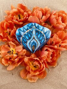 A Yoni Mandala featuring a blue candle and orange tulips amidst sand.