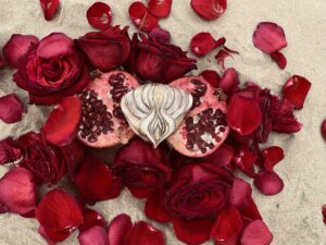 A Yoni Mandala holds a heart-shaped pomegranate on a bed of rose petals.