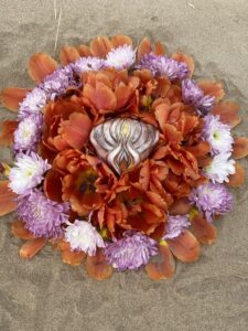 A Yoni Mandala, consisting of orange and purple flowers, adorns the sand.