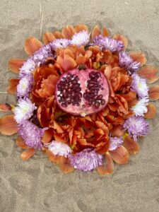 A Yoni Mandala of pomegranates rests on the sand.