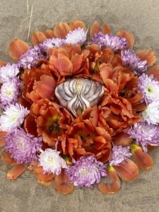 A Yoni Mandala of orange and purple flowers on the sand.