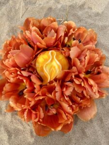 A Yoni Mandala of vibrant orange flowers resting on the sand.