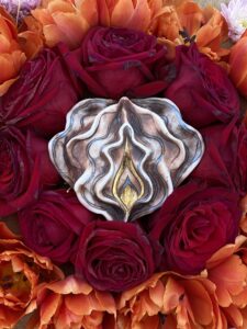 An image of a Yoni Mandala flower surrounded by a silver brooch.