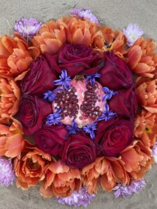 A Yoni Mandala of orange and purple flowers on the sand.