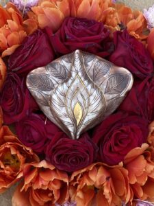 A Yoni Mandala adorned with a silver ring and vibrant orange flowers.