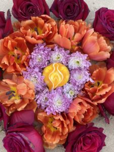 A Yoni Mandala made of orange and purple flowers in the sand.