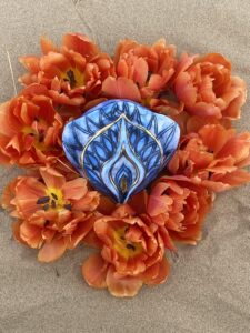 A Yoni Mandala featuring a blue stone amidst vibrant orange flowers on sandy grounds.