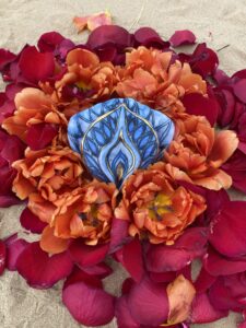 A blue Yoni Mandala flower resting on the sandy surface.